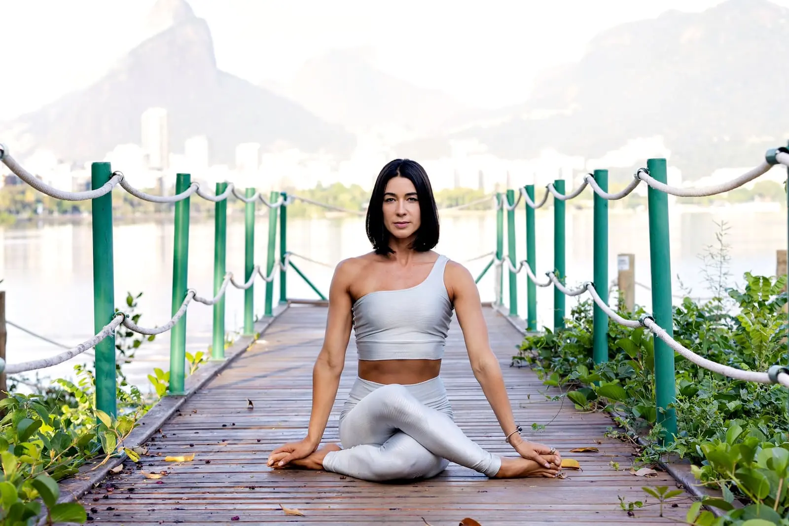 Dany Langer praticando yoga em um píer, com a paisagem do Rio de Janeiro ao fundo